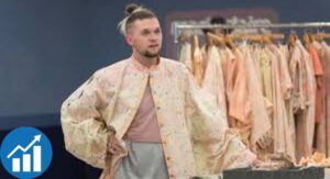 A Brandon Kee in a pink robe stands next to a clothing rack, which holds several different outfits.