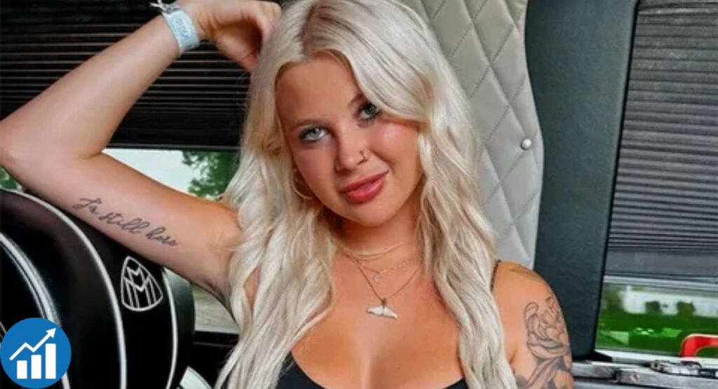 Christen Whitman posing inside a vehicle with visible arm tattoos and long blonde hair