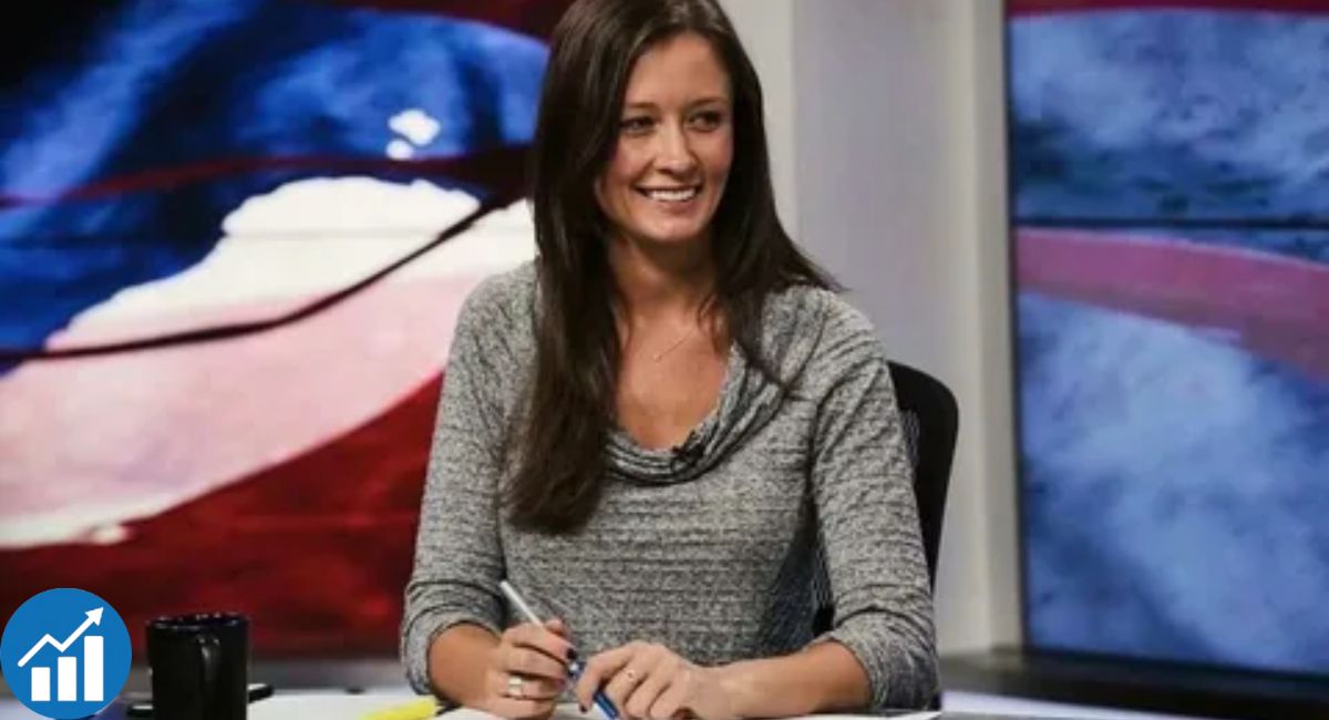 Emma Vigeland seated at a news desk, smiling during a live broadcast with political graphics in the background.